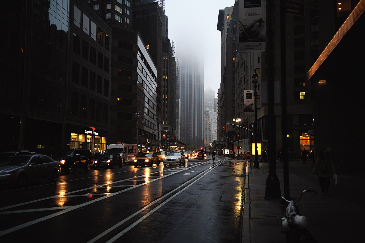 A rain-soaked city street with lights reflected on the road.