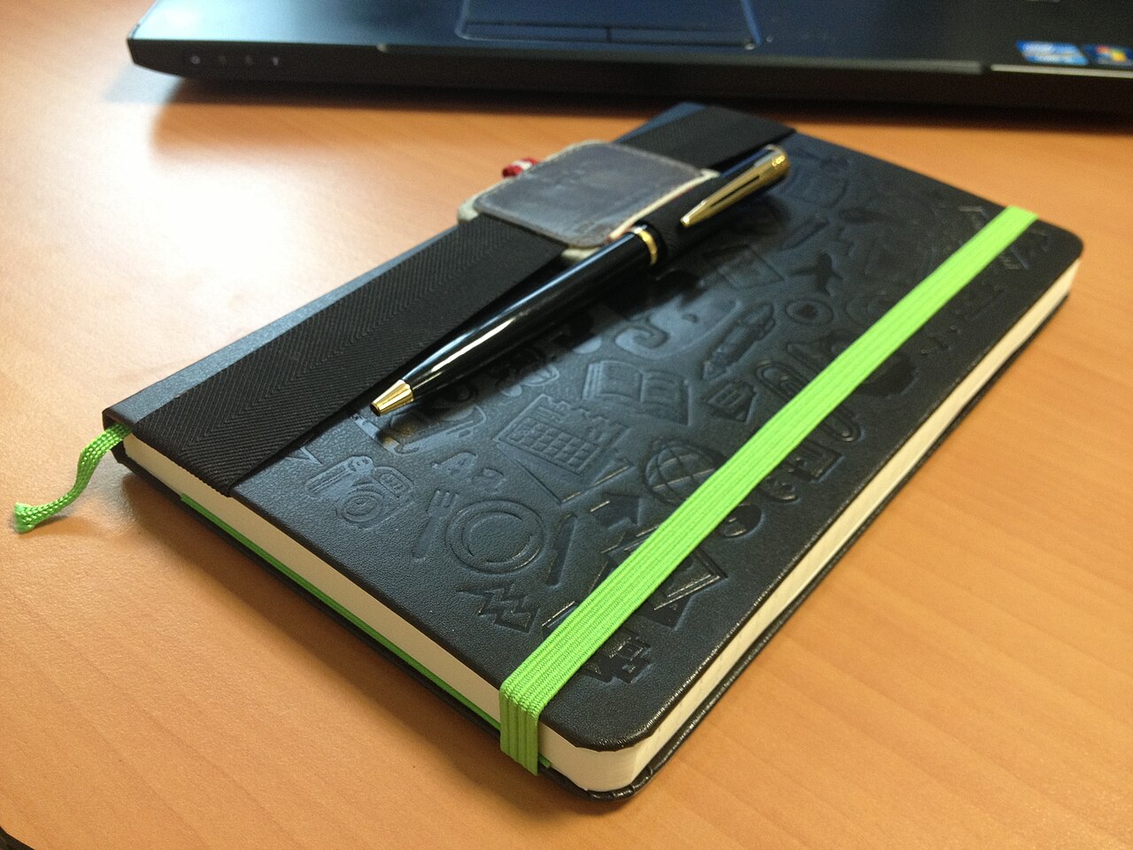 A closed notebook with a pen and a green bookmark ribbon.