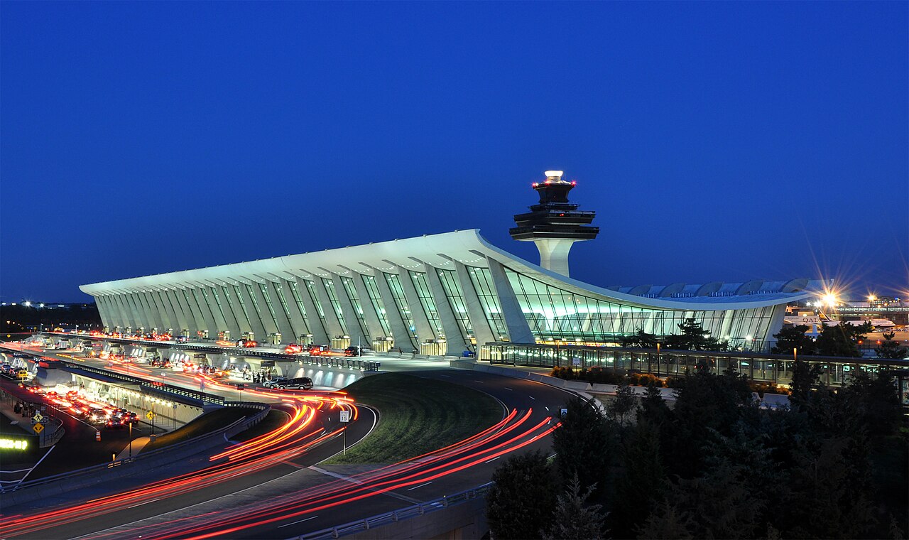 An illuminated airport terminal with evening traffic outside.