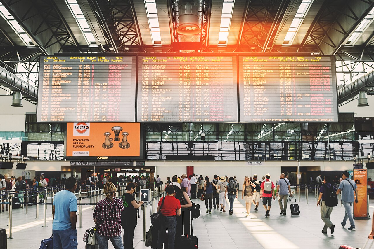 A large flight information display in a Prague airport hall.