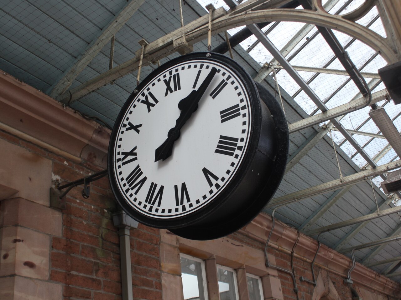 A large analogue clock beneath a railway platform roof.