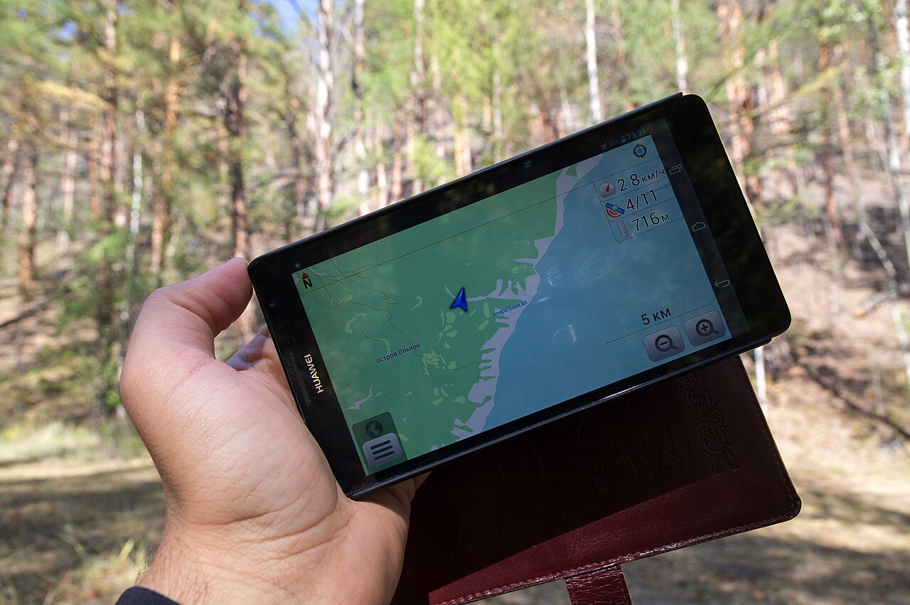 Kézben tartott telefon térképes navigációval egy erdős tájon.
