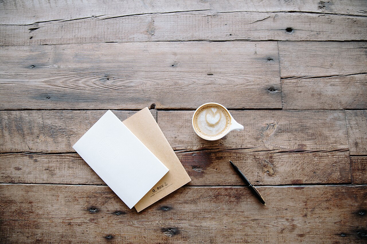 An open blank notebook and a cup of coffee on a wooden table.