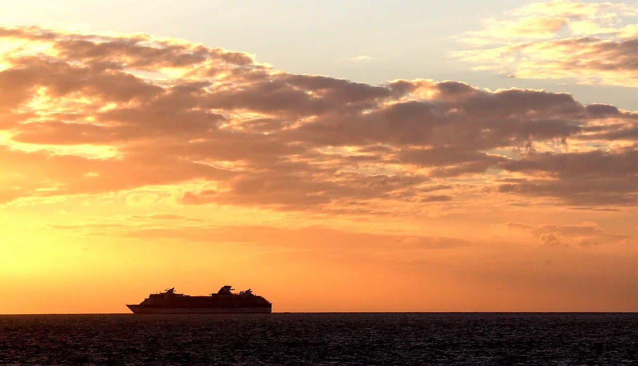 The silhouette of a cruise ship beneath a golden sunset.