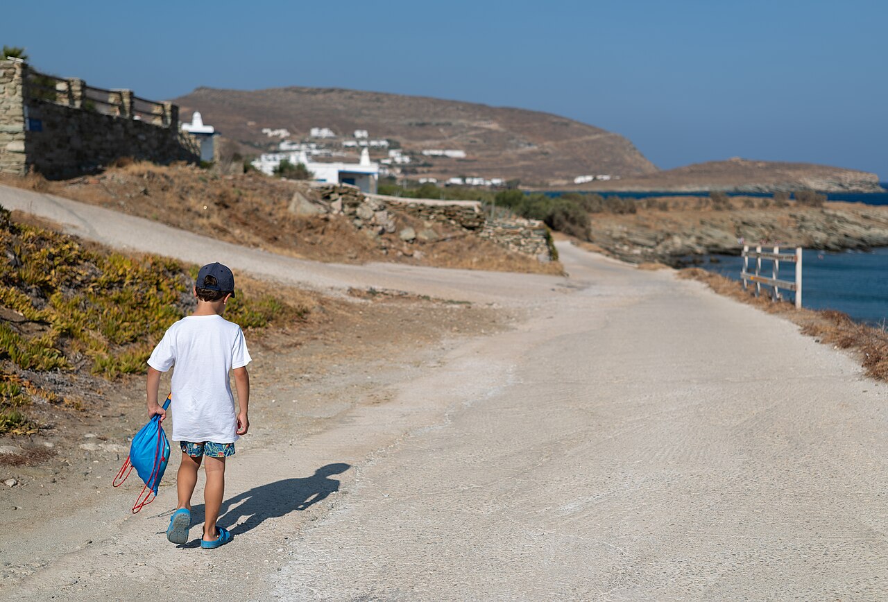 A person walking towards the beach carrying a light bag.