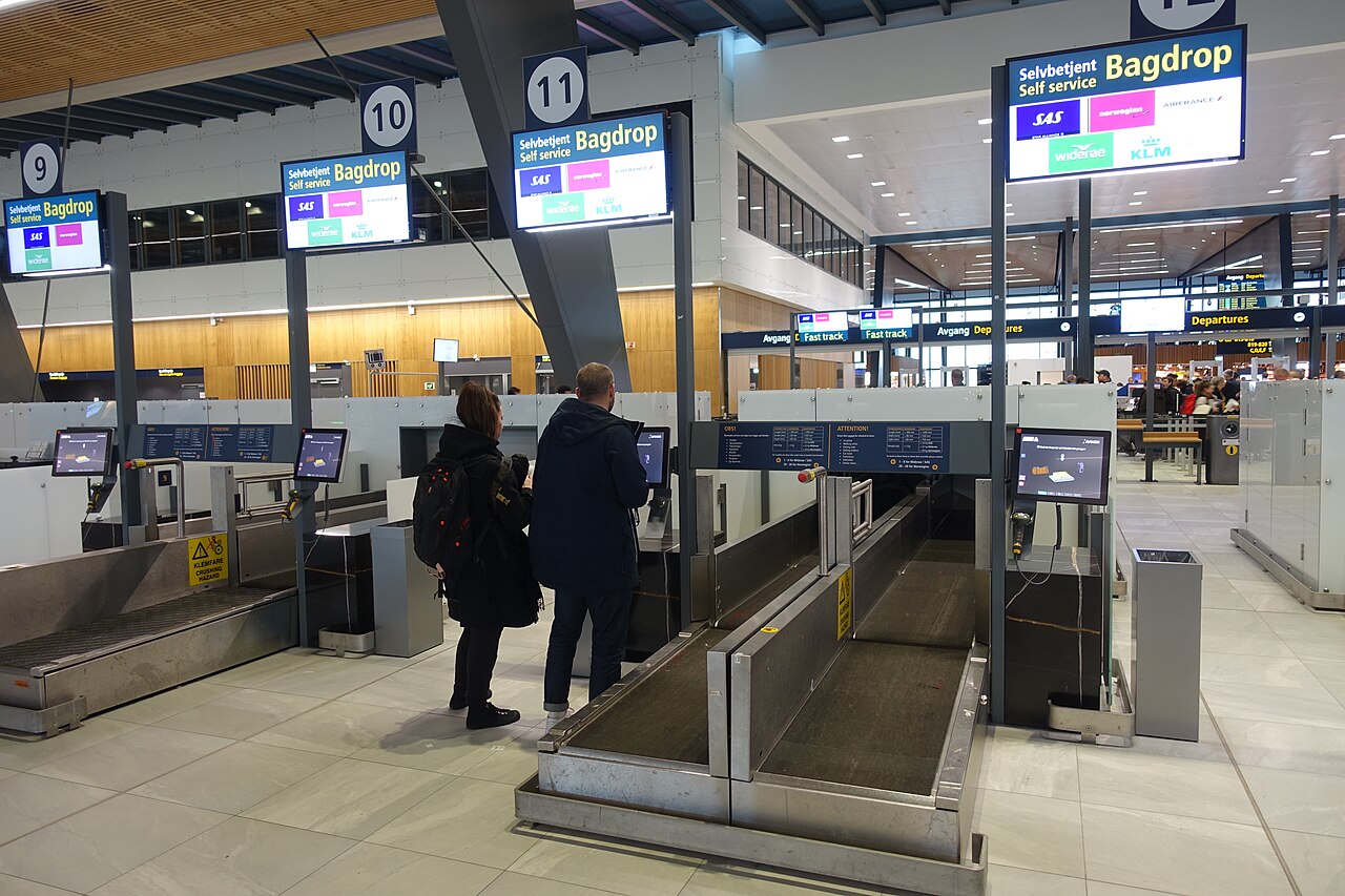 Self-service baggage-drop counters in an airport hall.