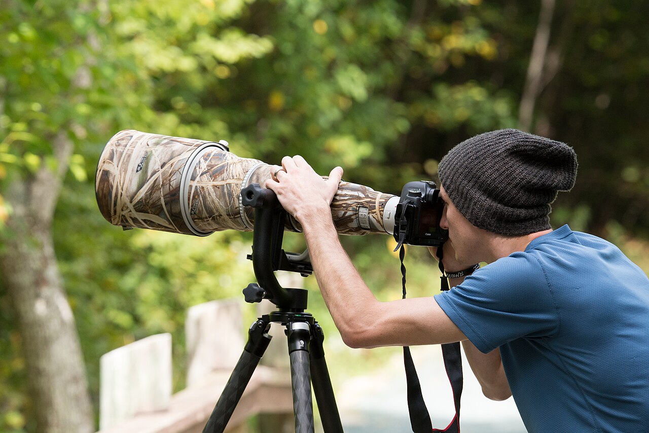 A photographer using a tripod-mounted camera outdoors.