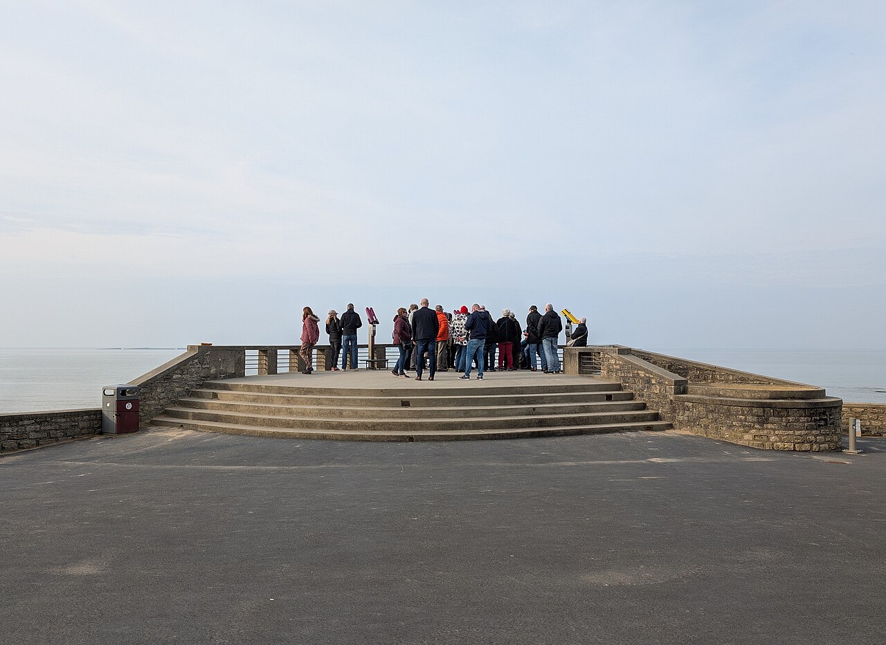 A group of travellers on the steps of a coastal viewpoint.