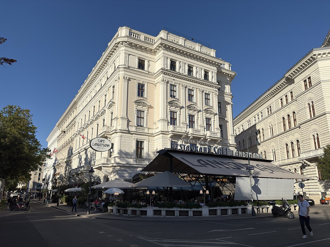 The terrace of a Viennese café outside a bright building.