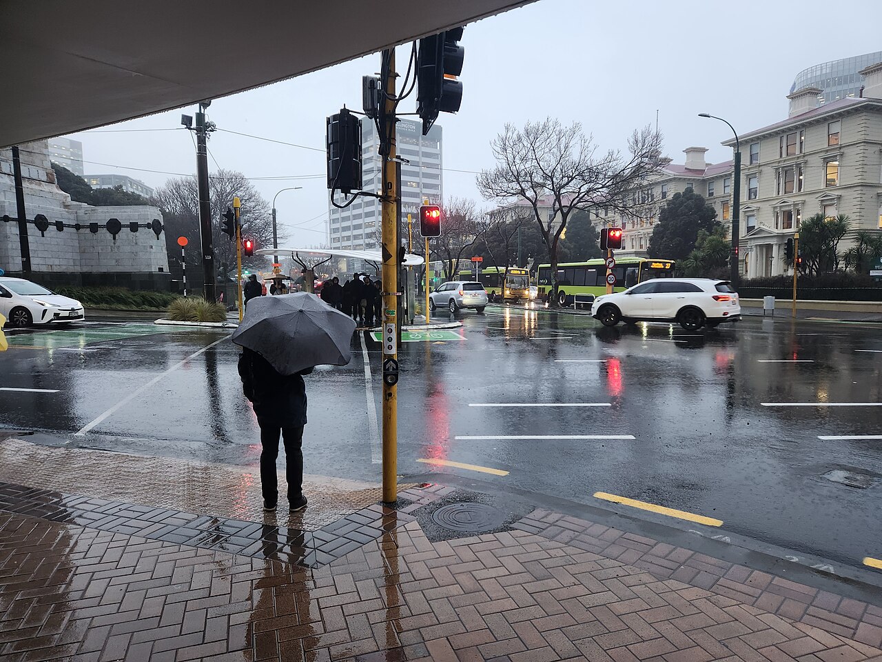 A pedestrian with an umbrella waiting at a rainy city junction.